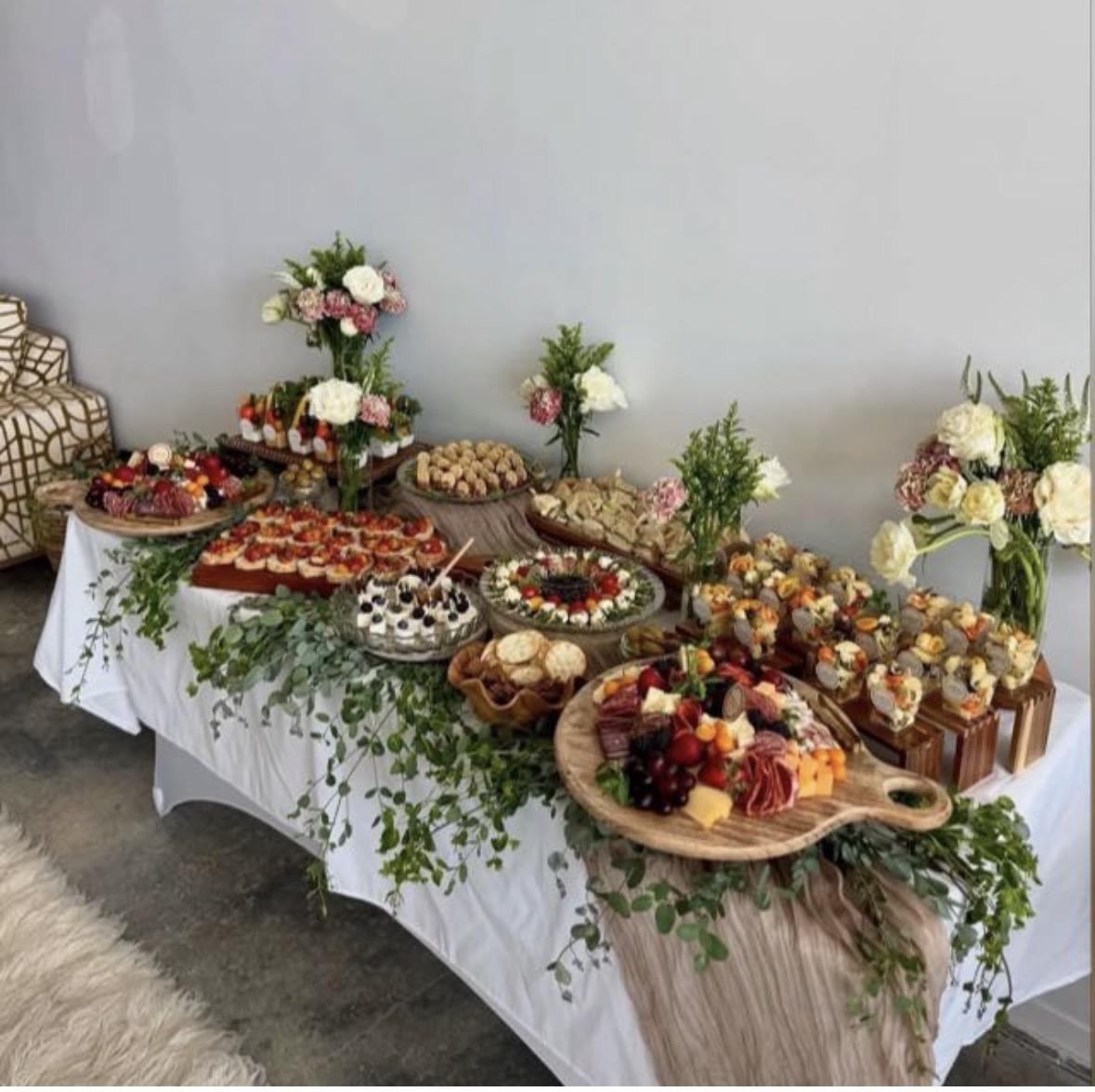 Grazing table by Aura Gourmet with charcuterie boards, appetizers and white flowers at a private event