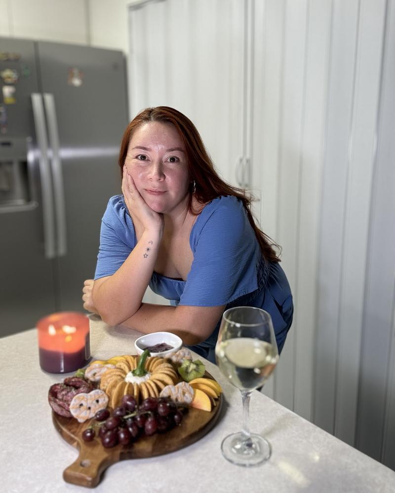 Laura, co-founder of Aura Gourmet, at the kitchen counter next to a charcuterie board and a glass of white wine